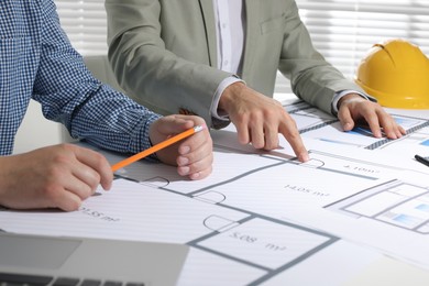 Architects working with construction drawings at table in office, closeup