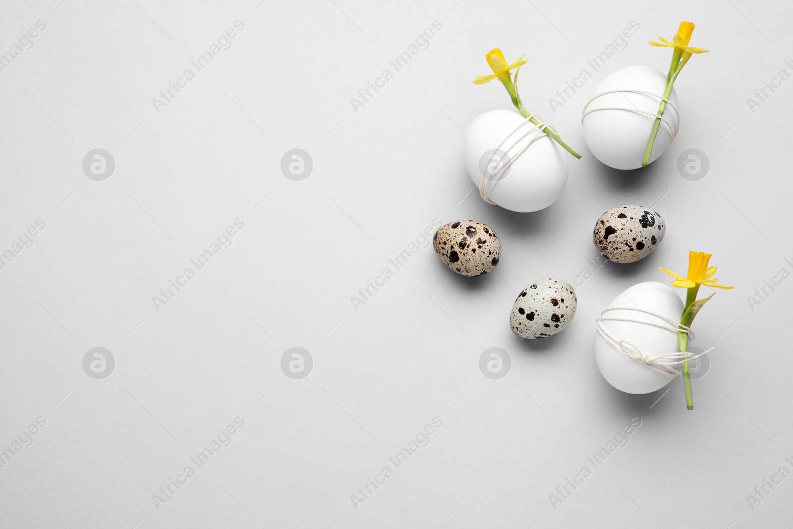 Photo of Easter eggs decorated with flowers on light grey background, flat lay. Space for text