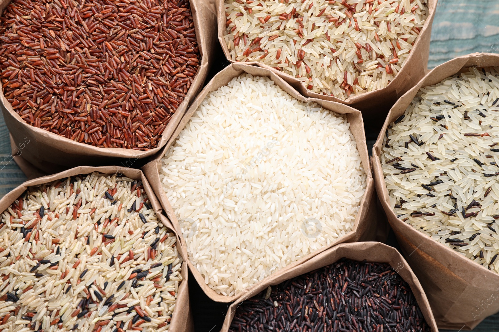 Photo of Brown and polished rice in paper bags on table, top view