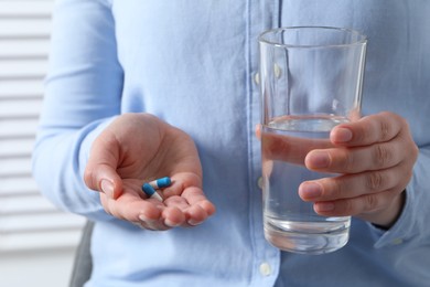Woman with glass of water and pill on blurred background, closeup