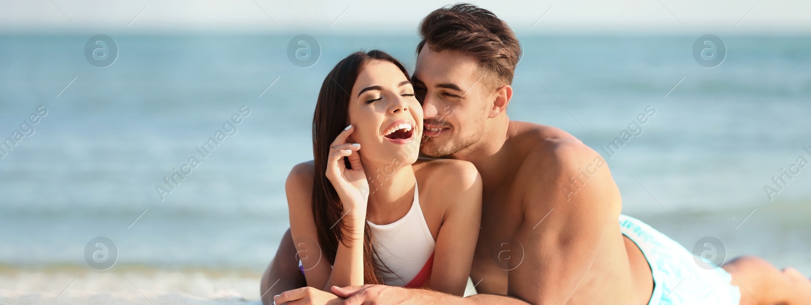 Image of Happy young couple lying together on beach. Banner design