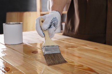 Photo of Man varnishing wooden surface with brush indoors, closeup
