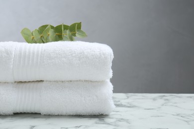Photo of Folded terry towels and eucalyptus branch on white marble table, closeup. Space for text