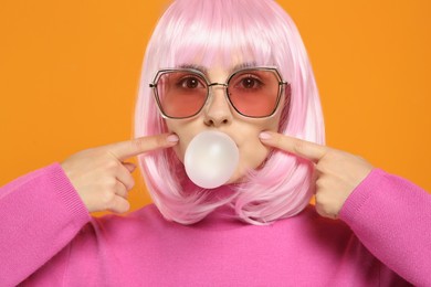 Photo of Beautiful woman in sunglasses blowing bubble gum on orange background