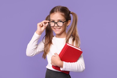 Photo of Smiling schoolgirl with book on violet background