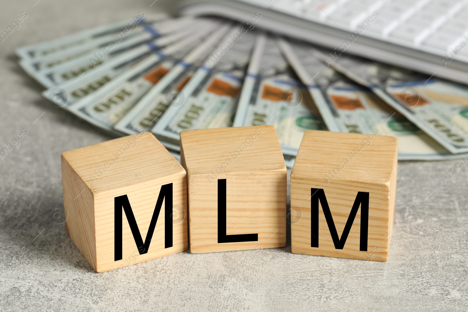 Image of Multi-level marketing. Abbreviation MLM of cubes with letters and dollar banknotes on grey table