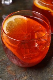 Photo of Aperol spritz cocktail, ice cubes and orange slice in glass on grey textured table, closeup