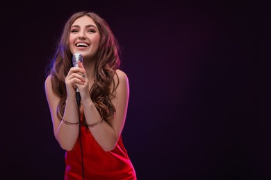 Photo of Emotional woman with microphone singing in color lights on black background. Space for text