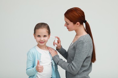 Photo of Mother spraying medication into daughter's ear on light grey background