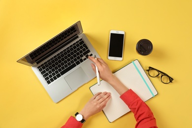 Photo of Woman working with modern laptop at color table, top view