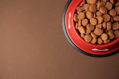 Photo of Dry dog food in feeding bowl on brown background, top view. Space for text