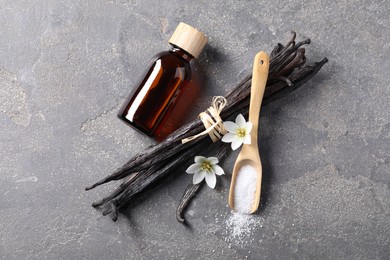 Photo of Spoon with sugar, flowers, vanilla pods and bottle of essential oil on grey textured table, flat lay