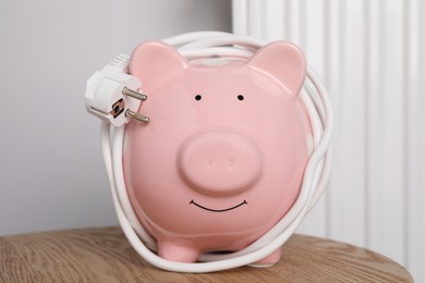 Photo of Piggy bank with plug on wooden table near heating radiator