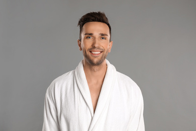 Happy young man in bathrobe on grey background