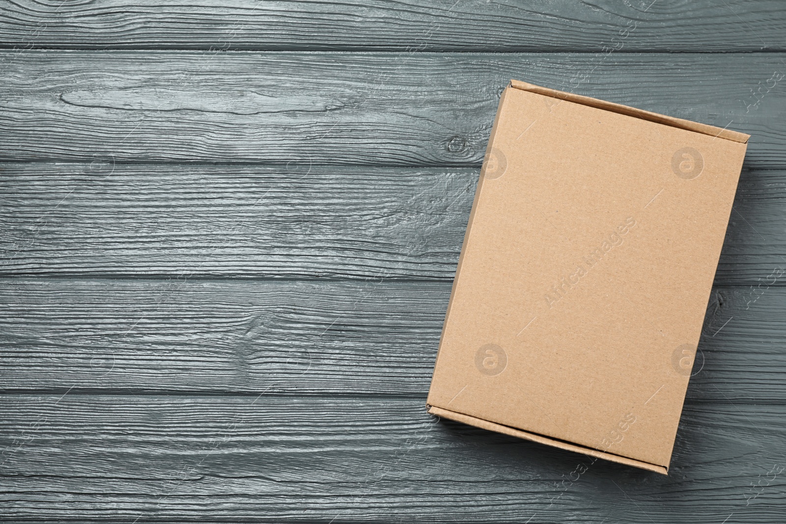 Photo of Closed cardboard box on grey wooden table, top view. Space for text