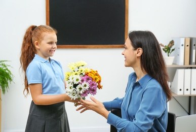 Photo of Schoolgirl congratulating her pedagogue with bouquet in classroom. Teacher's day