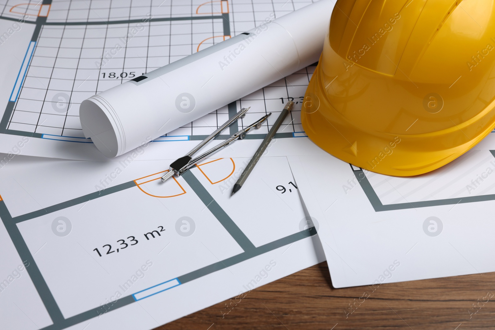 Photo of Construction drawings, safety hat, pair of compasses and pencil on wooden table