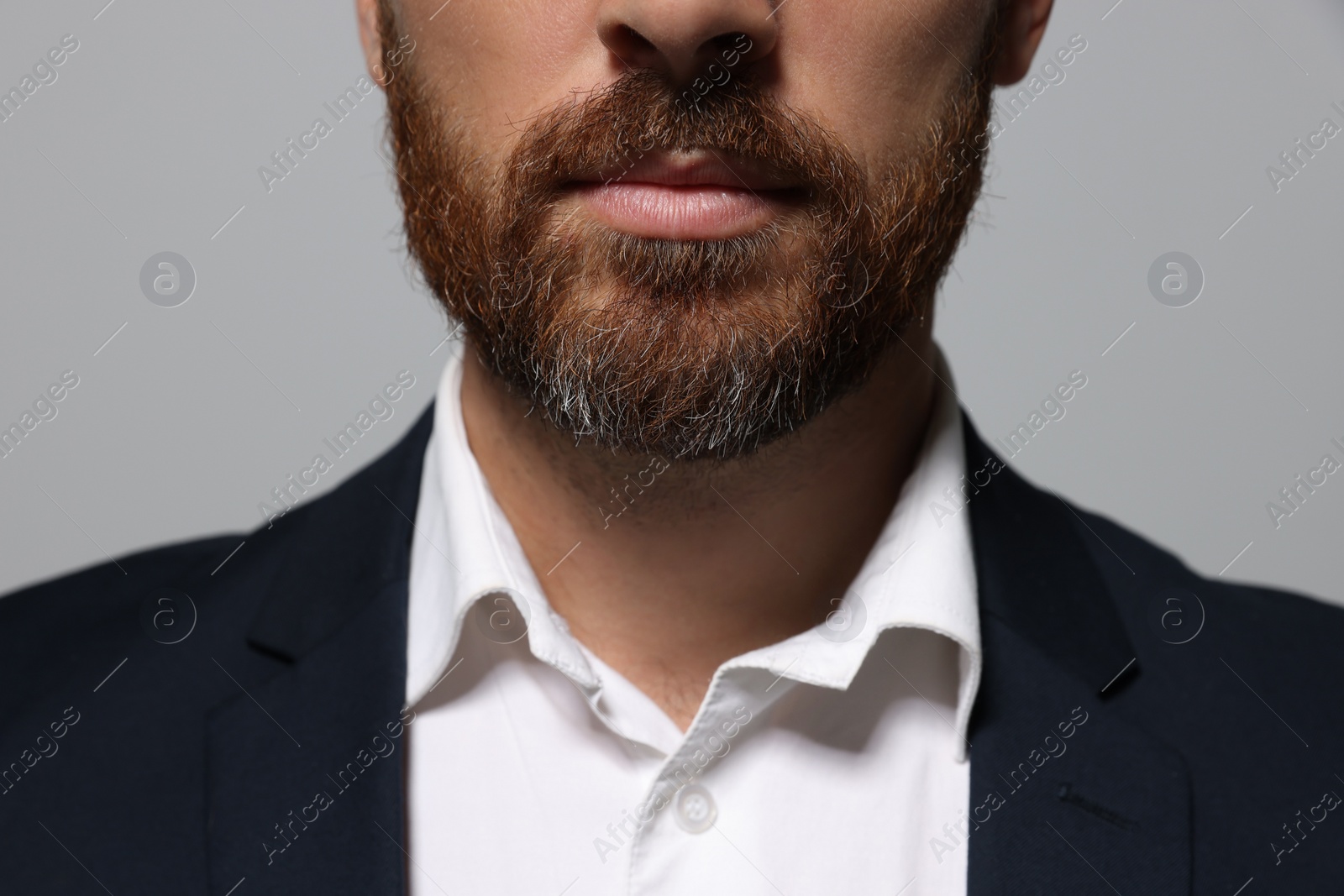 Photo of Handsome man with beard in suit on light grey background, closeup