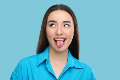 Photo of Happy woman showing her tongue on light blue background