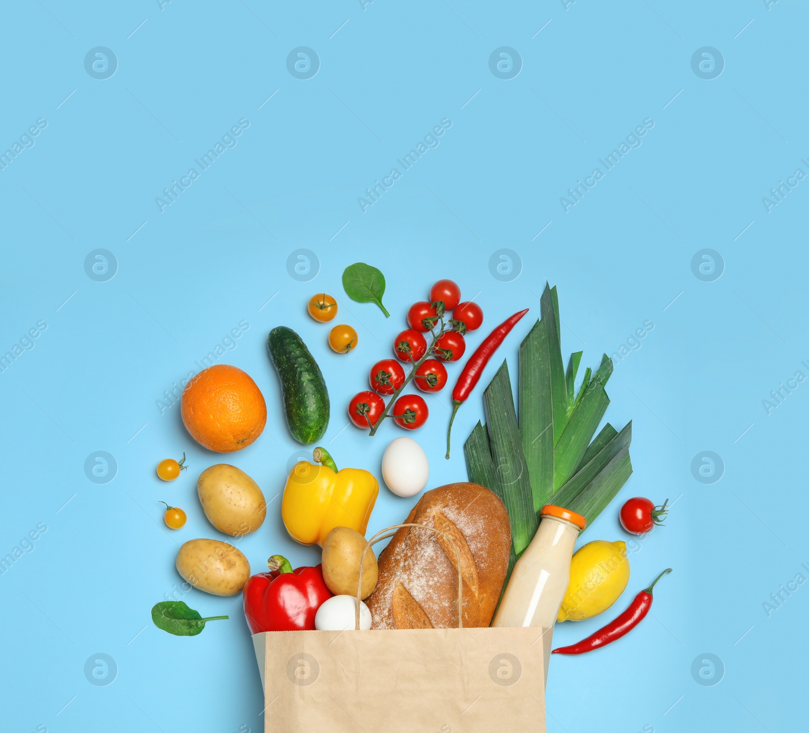 Photo of Shopping paper bag with different groceries on light blue background, flat lay