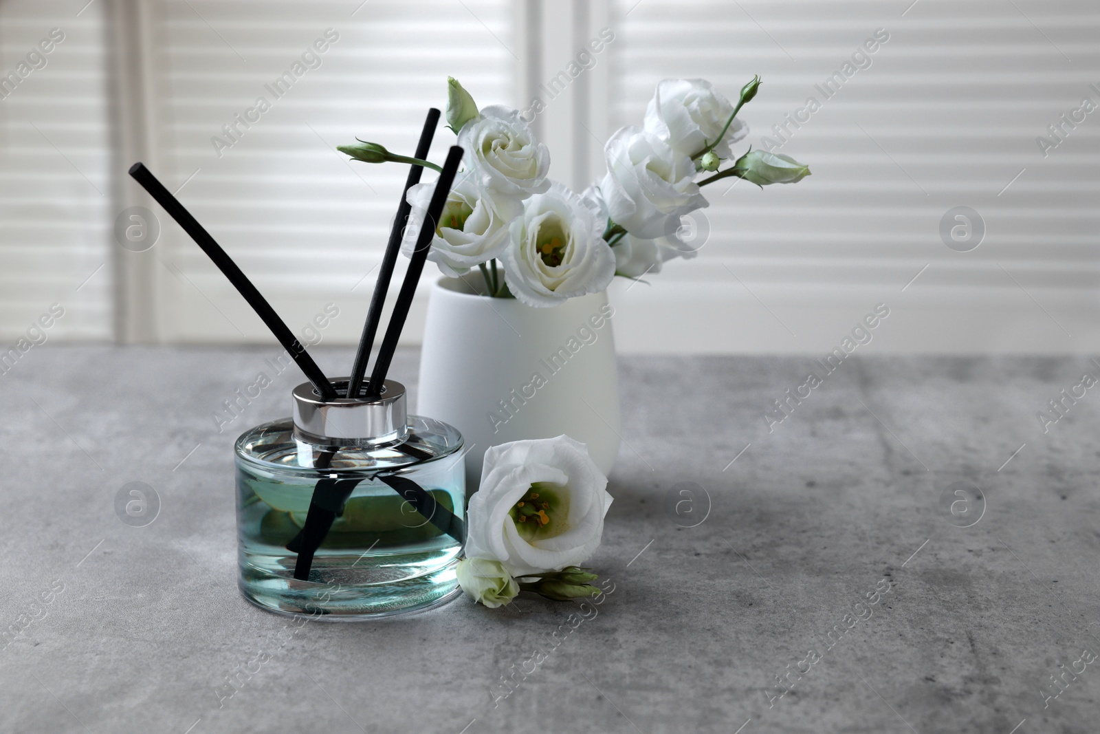 Photo of Reed diffuser and vase with eustoma flowers on gray marble table