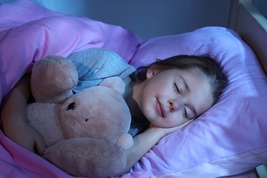 Photo of Cute little girl with toy bear sleeping in bed at home