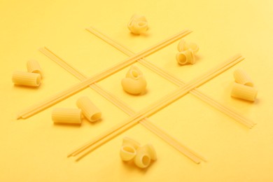 Tic tac toe game made with different types of pasta on yellow background