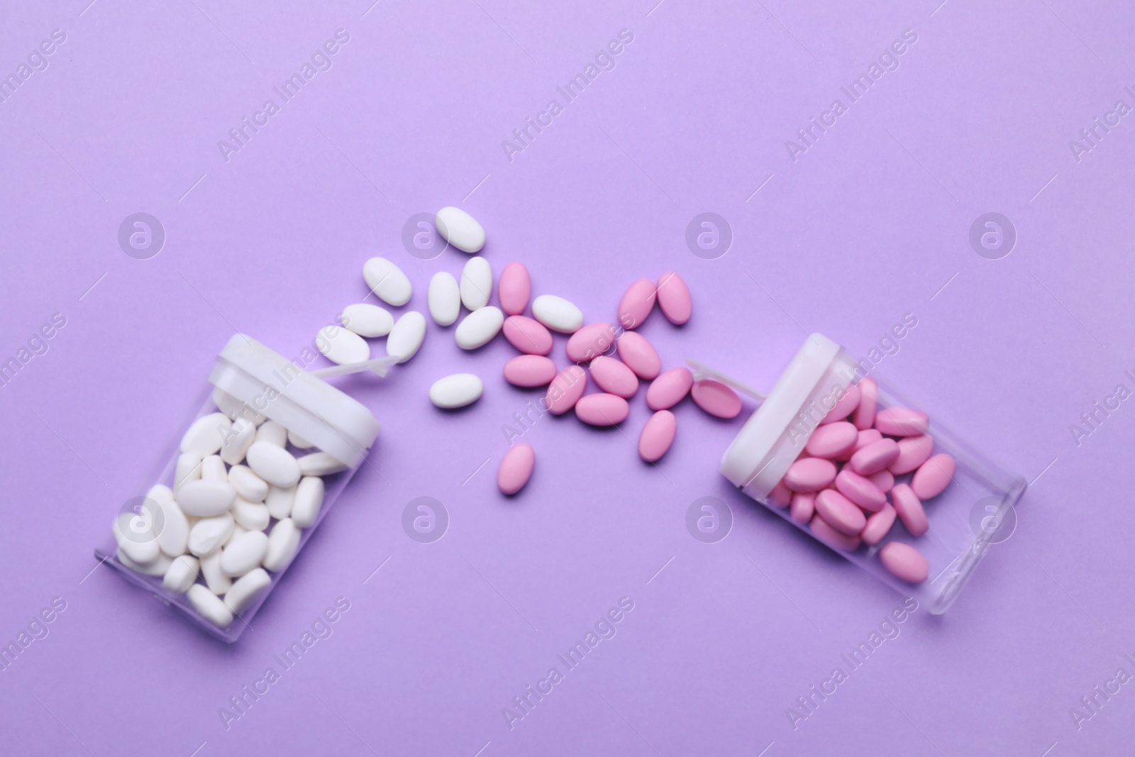 Photo of Containers and different dragee candies on lilac background, flat lay