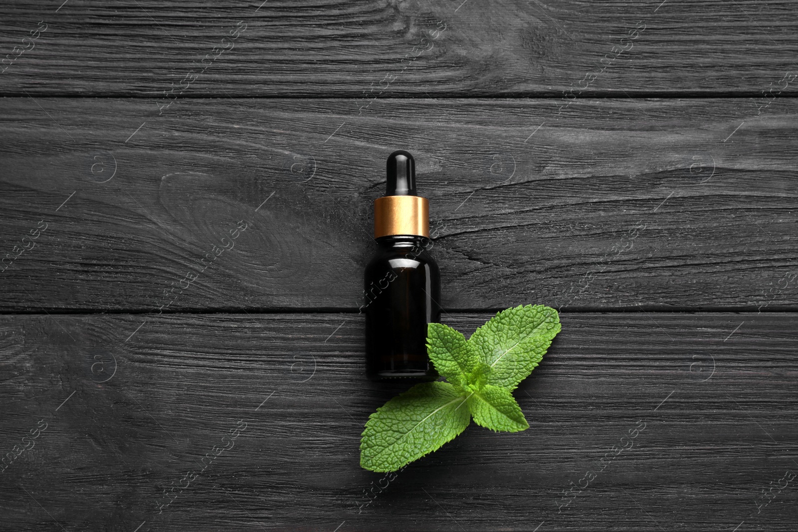 Photo of Bottle of mint essential oil and green leaves on black wooden table, flat lay