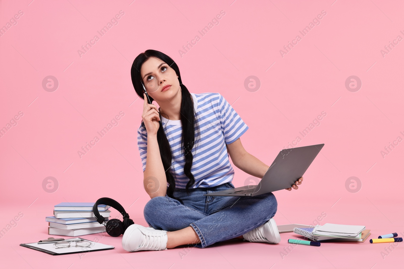 Photo of Student with laptop sitting among books and stationery on pink background