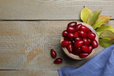 Photo of Fresh ripe dogwood berries with green leaves on wooden table, flat lay. Space for text