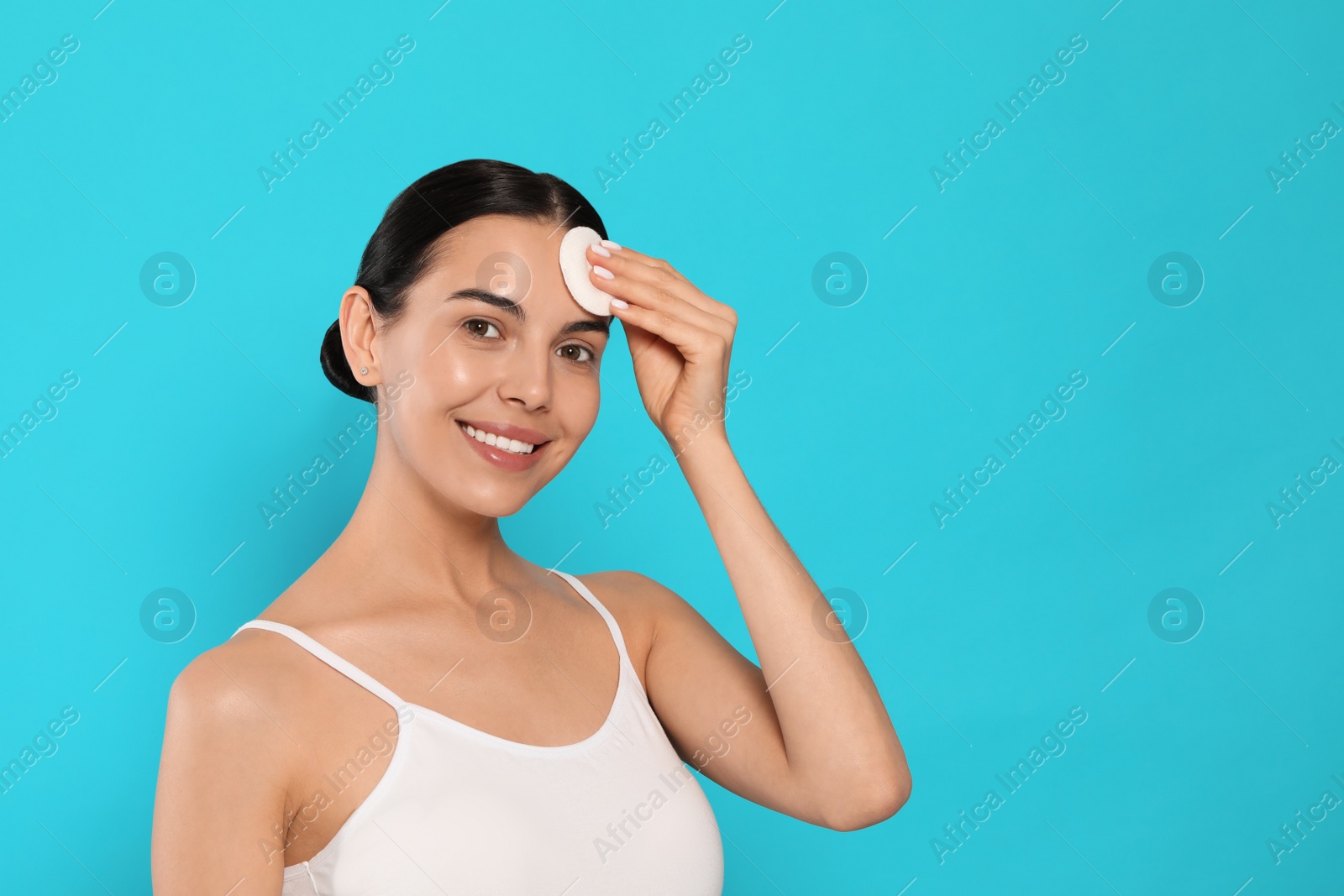 Photo of Young woman using cotton pad with micellar water on light blue background, space for text