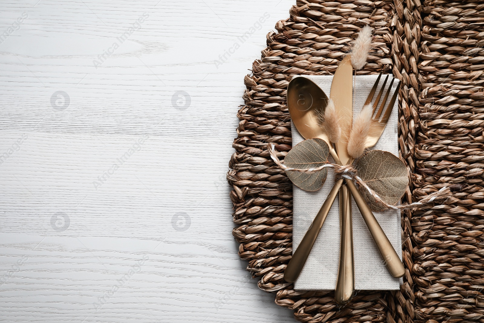 Photo of Autumn table setting, space for text. Cutlery and wicker mat on white wooden background, flat lay