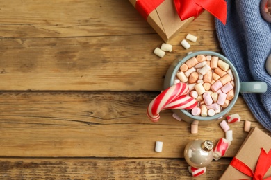 Photo of Flat lay composition with cup of tasty cocoa, candy canes and Christmas gifts on wooden table, flat lay. Space for text