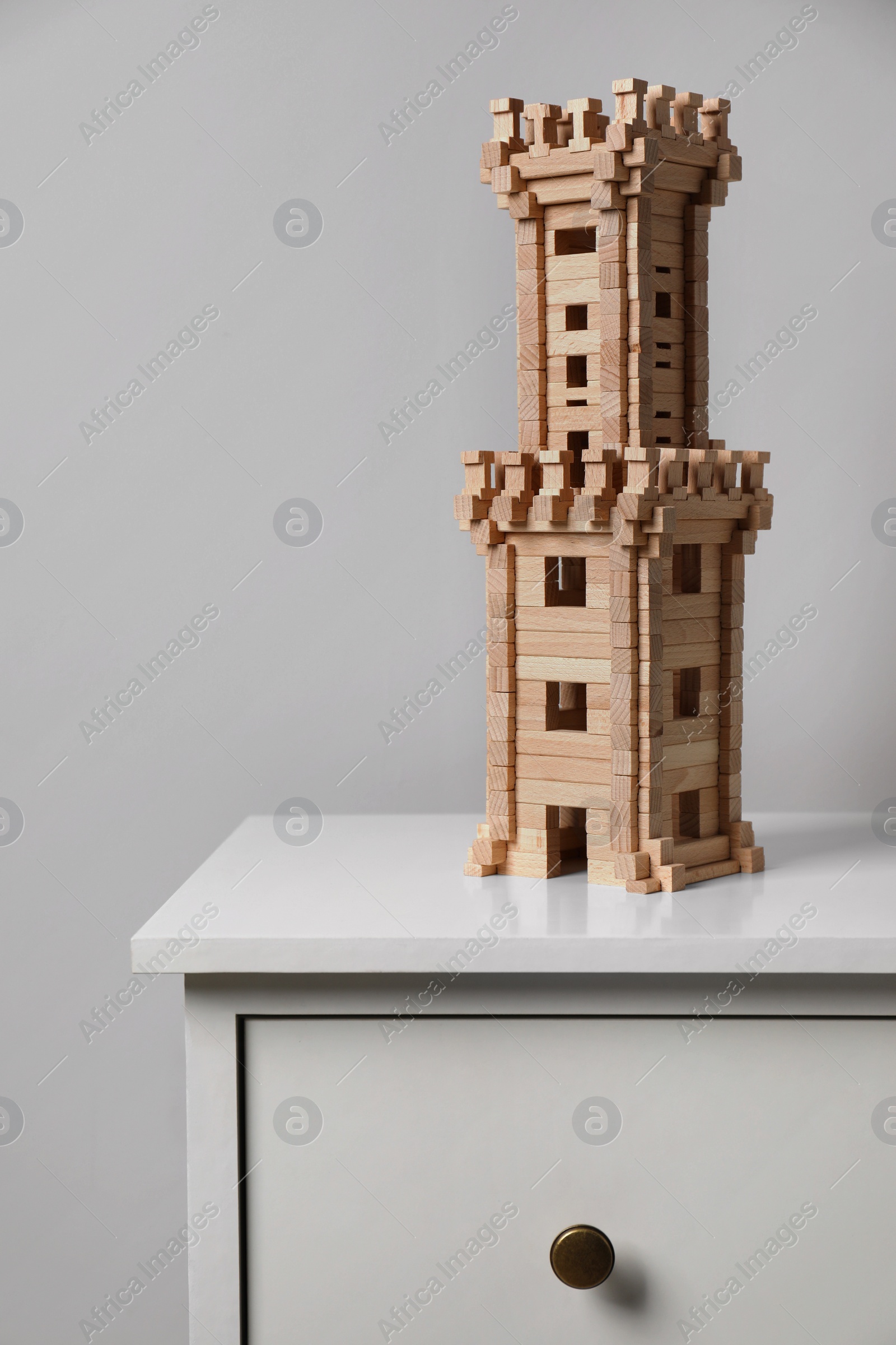 Photo of Wooden tower on chest of drawers near light grey wall. Children's toy