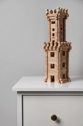 Wooden tower on chest of drawers near light grey wall. Children's toy