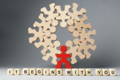 Photo of Recruitment and team work concept. Phrase It Begins With You made of cubes, red human figure among wooden ones on light grey background