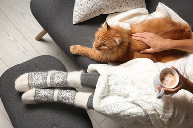 Photo of Woman with cute red cat and coffee on grey sofa at home, top view