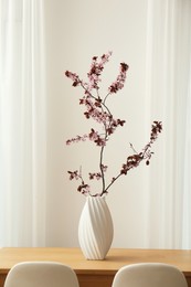 Photo of Blossoming tree twig in vase on wooden table indoors