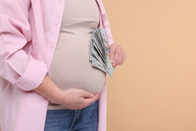 Photo of Surrogate mother. Pregnant woman with dollar banknotes on beige background, closeup. Space for text