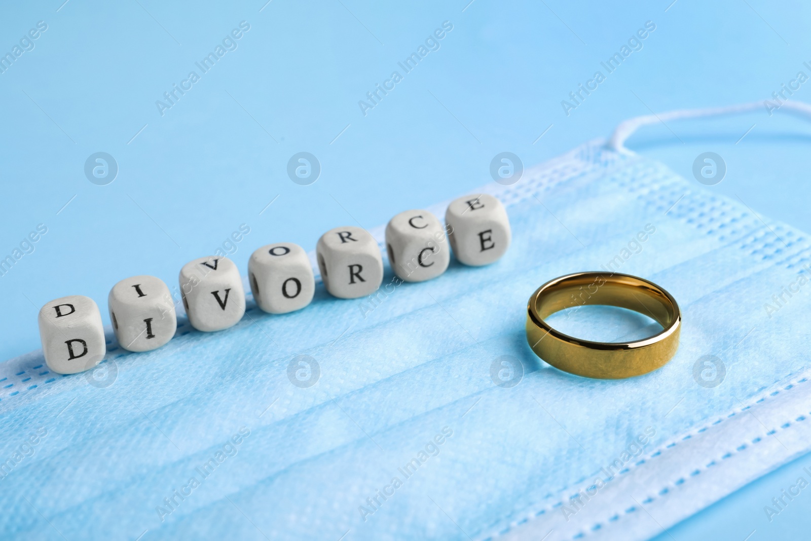Photo of Wooden cubes with word Divorce, wedding ring and medical mask on light blue background, closeup. Breaking family ties during coronavirus outbreak