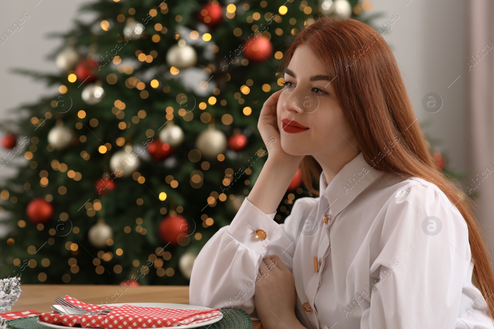 Photo of Beautiful young woman near Christmas tree at table in room, space for text
