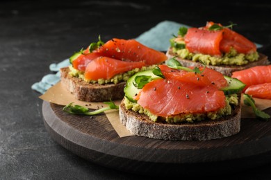 Photo of Tasty bruschettas with salmon, guacamole and microgreens on black table, closeup