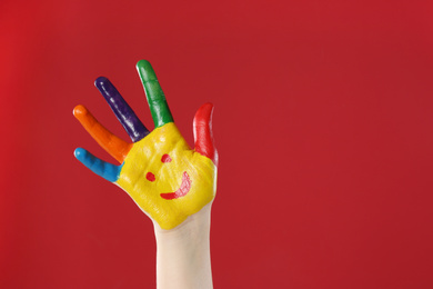 Photo of Kid with smiling face drawn on palm against red background, closeup. Space for text