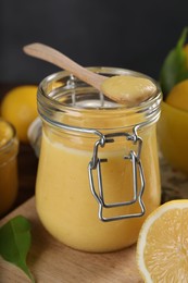 Delicious lemon curd in glass jar, spoon and fresh citrus fruit on table