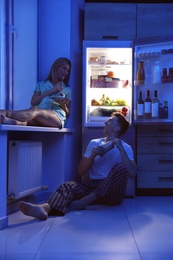 Happy couple eating near refrigerator in kitchen at night