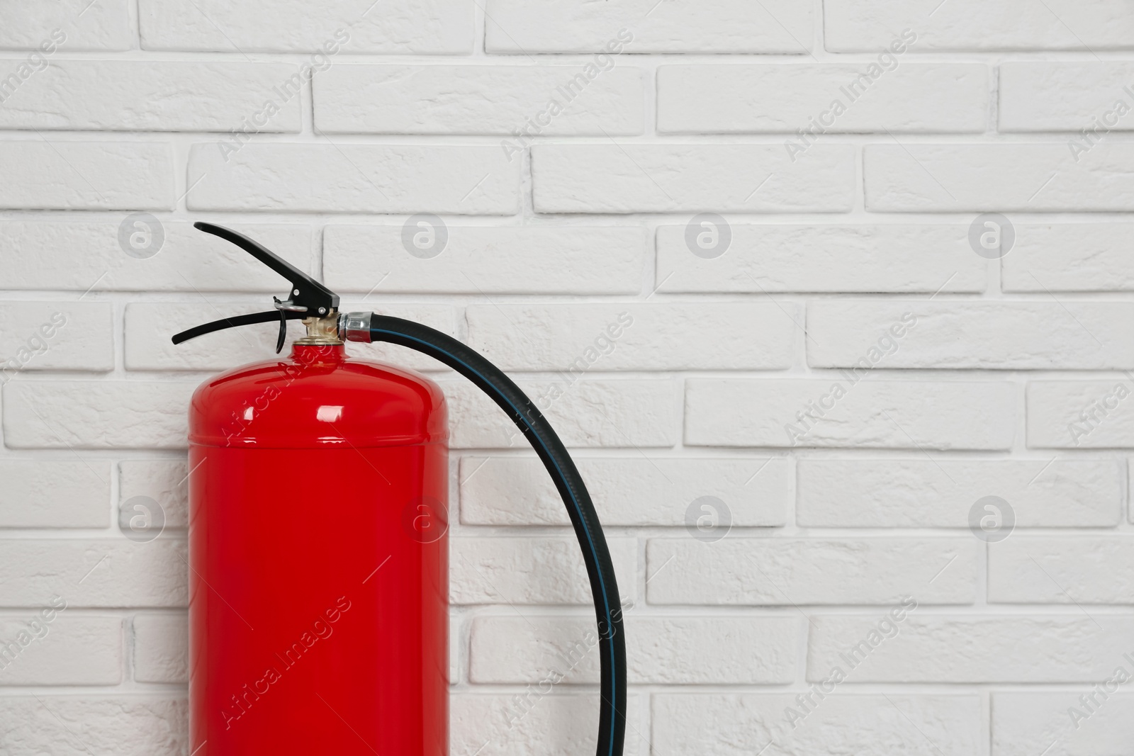 Photo of Fire extinguisher near white brick wall, closeup. Space for text