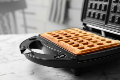 Photo of Modern iron with tasty Belgian waffles on white marble table, closeup