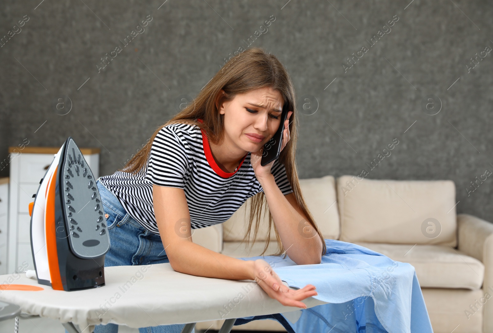 Photo of Emotional woman talking on phone while ironing clothes at home