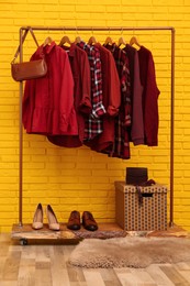 Rack with stylish clothes and bag near yellow brick wall indoors